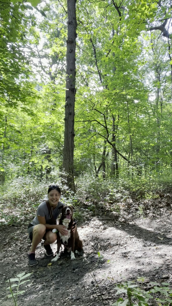 Joyce crouching with a dog on a forest trail